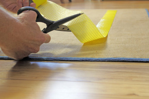 Man cutting and applying an anti-skid carpet tape on area rug.