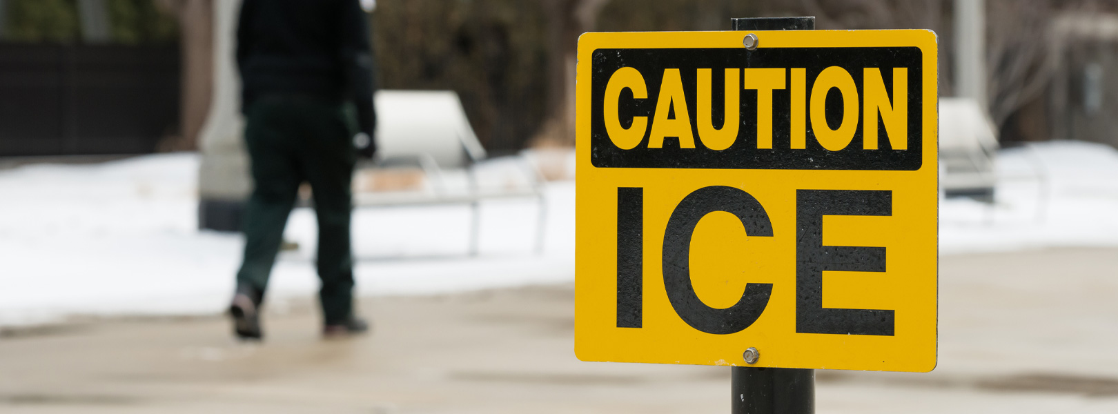 "CAUTION ICE" sign and man walking on sidewalk in the distance
