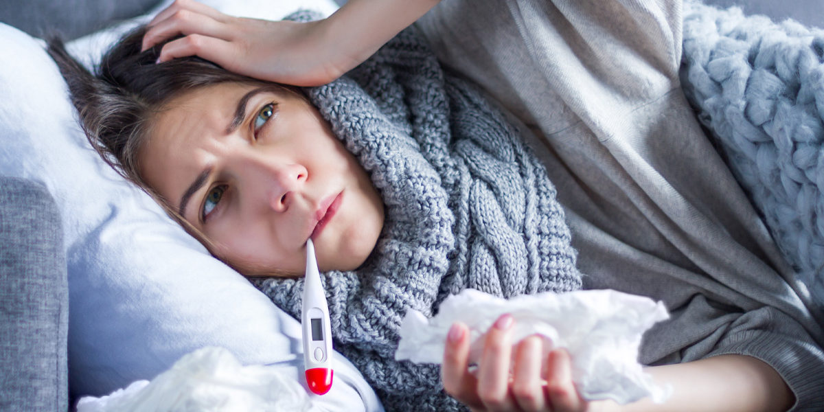 Under the weather woman on couch taking her temperature.