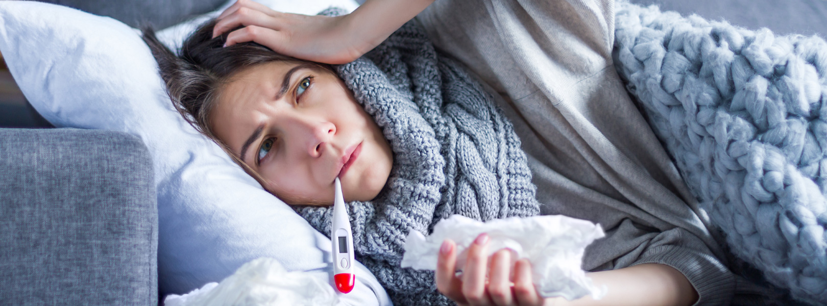 Under the weather woman on couch taking her temperature.