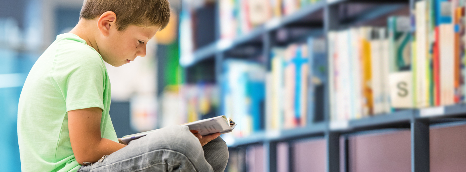 little boy in a green shirt reading a book in a library