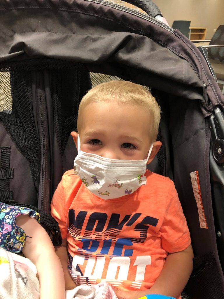 3-year-old boy with blonde hair wearing a surgical mask in a stroller 