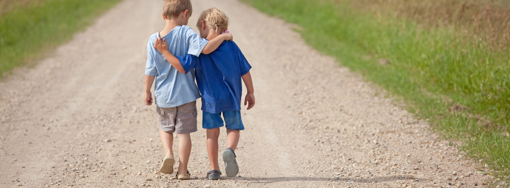 Two boys walking down a dirt road, arms around each others shoulders