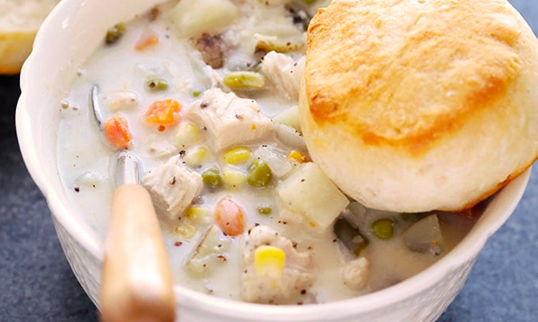 A bowl of chicken pot pie soup and biscuit