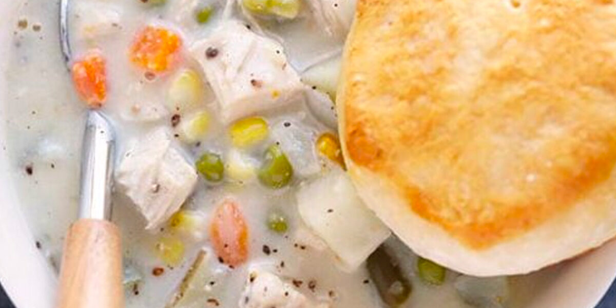 Close up image of a bowl of chicken pot pie soup and biscuit