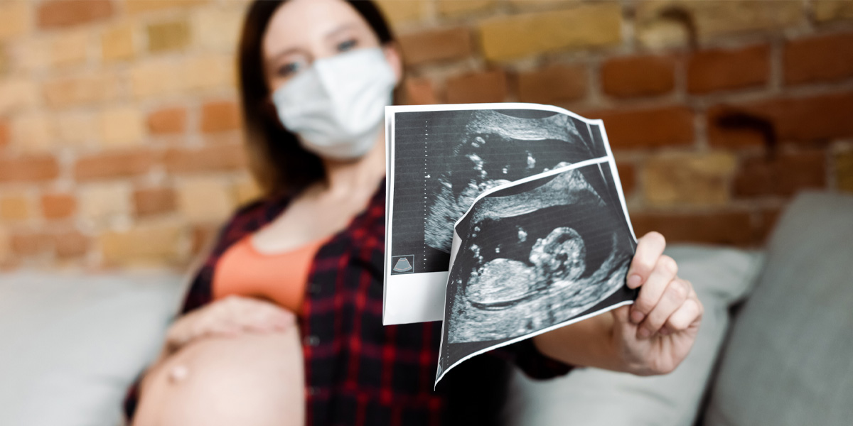 Pregnant women, wearing mask, showing off ultrasounds of her baby