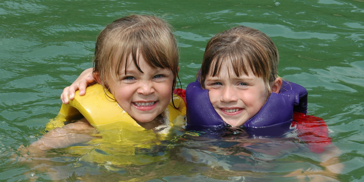 Two girls, with lifejackets, swimming in a lake