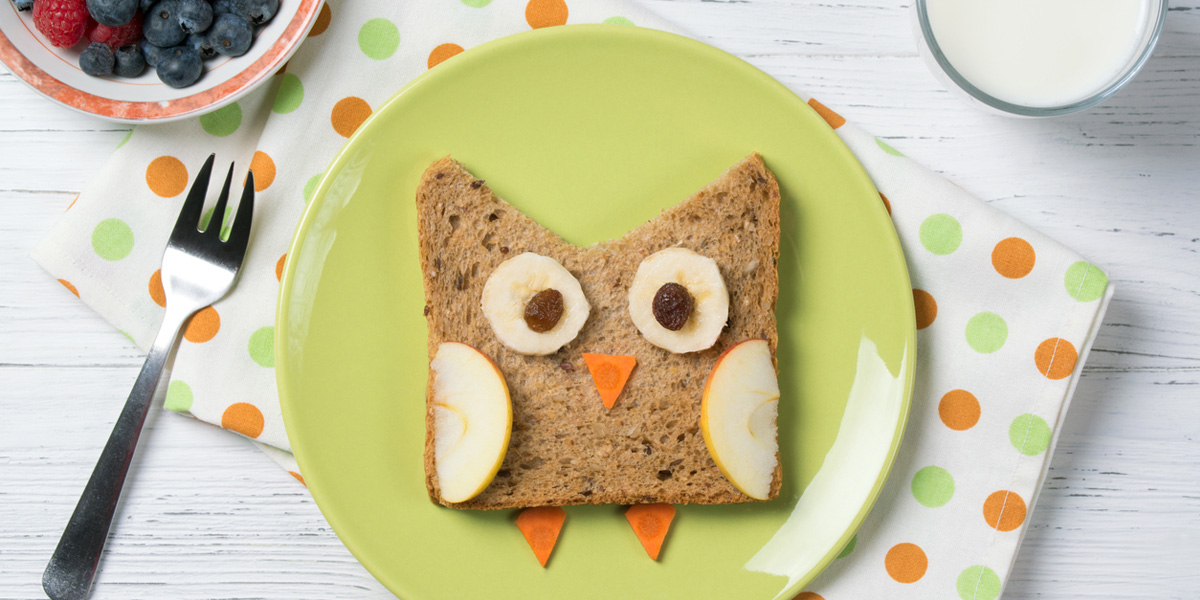 a sandwich shaped like an owl on a color plate, along with a glass of milk and bowl of berries