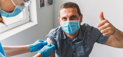 Man wearing a mask and giving the thumbs-up sign after getting a vaccine