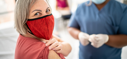 Woman with red face mask rolling up her sleeve for a vaccine