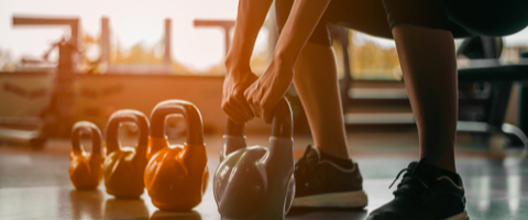 person squatting to pick up a kettlebell at the end of a row of four kettlebells