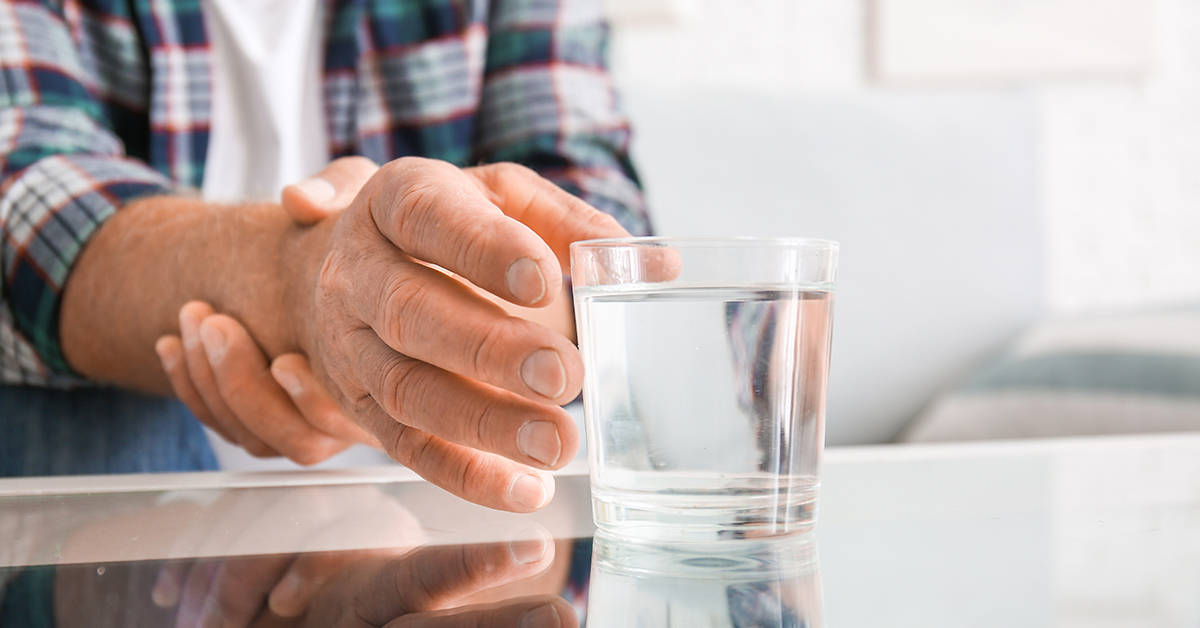 A man holding his hand steady as he reaches for a glass of water