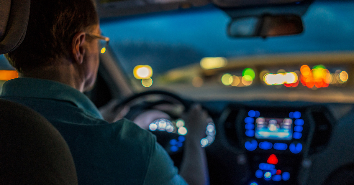 A man driving at night, blurred lights in the distance