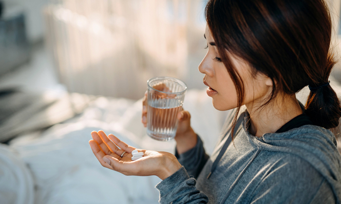 Woman holding pills in one hand and glass of water in the other