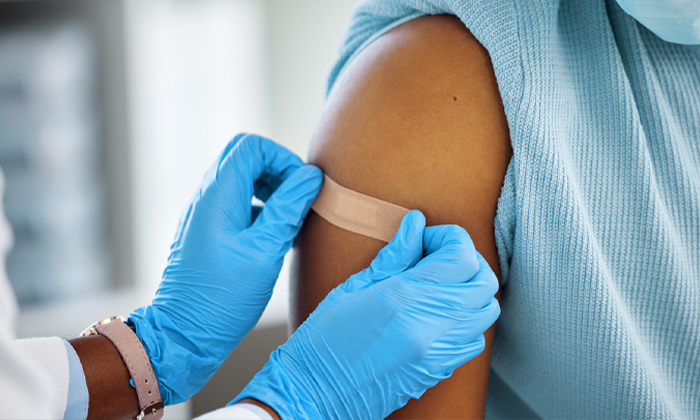 Healthcare provider placing bandage on patient's arm after vaccination