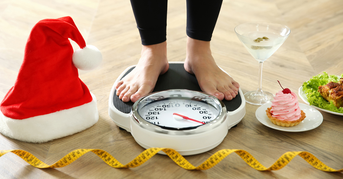 Food, alcohol left after Christmas holidays and woman with measuring tape standing on scales indoors