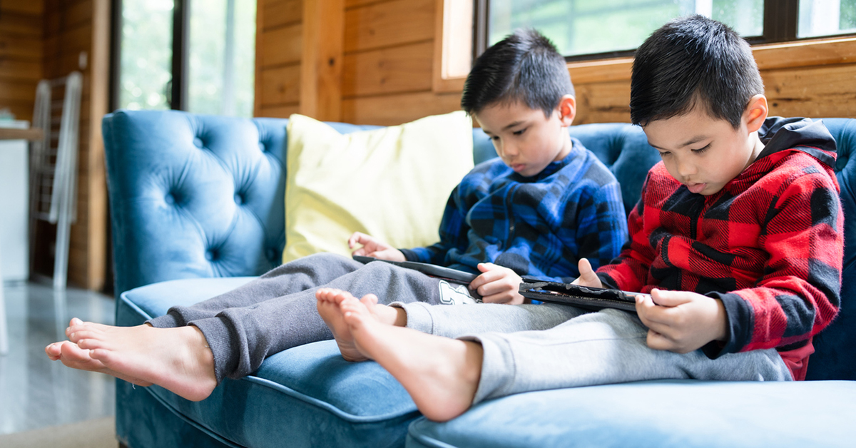Two young boys sitting on a couch playing with mobile devices