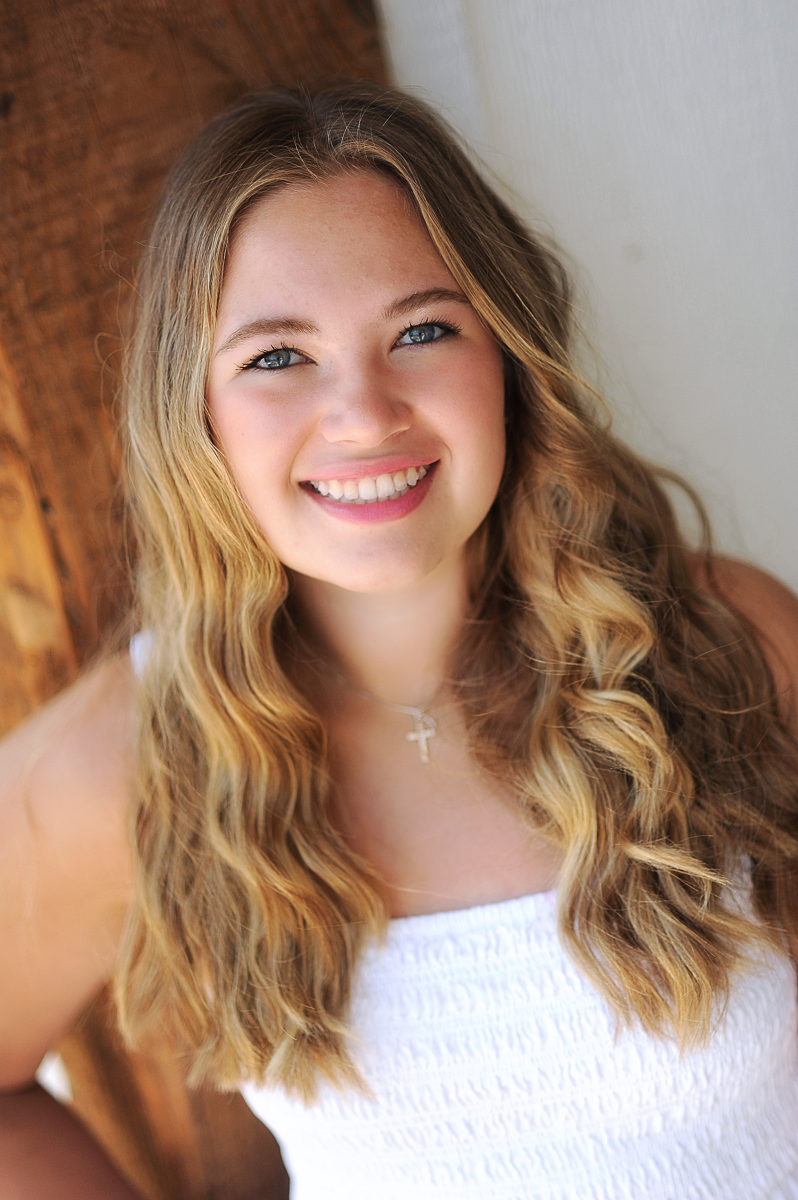 Young lady smiling with long blondish-brown hair wearing a Christian cross necklace and smiling with her teeth showing. 