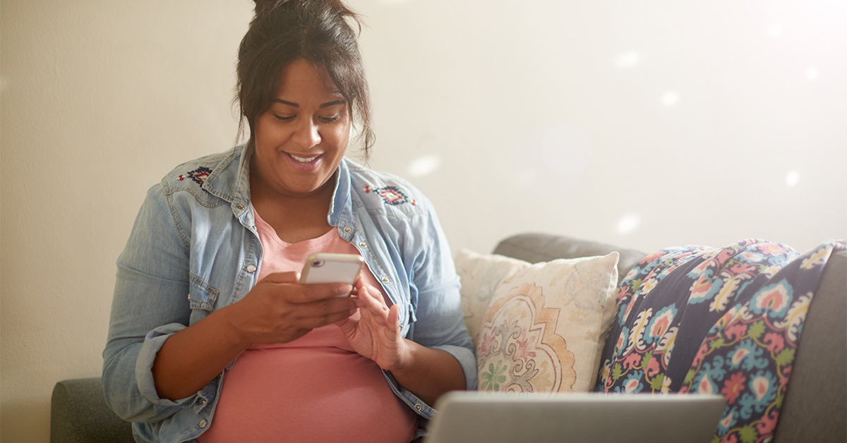 Pregnant woman sitting on couch on her phone