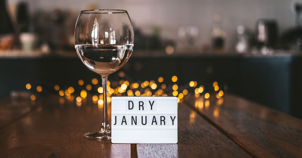 Wine glass on wood table with twinkling lights and sign that reads Dry January
