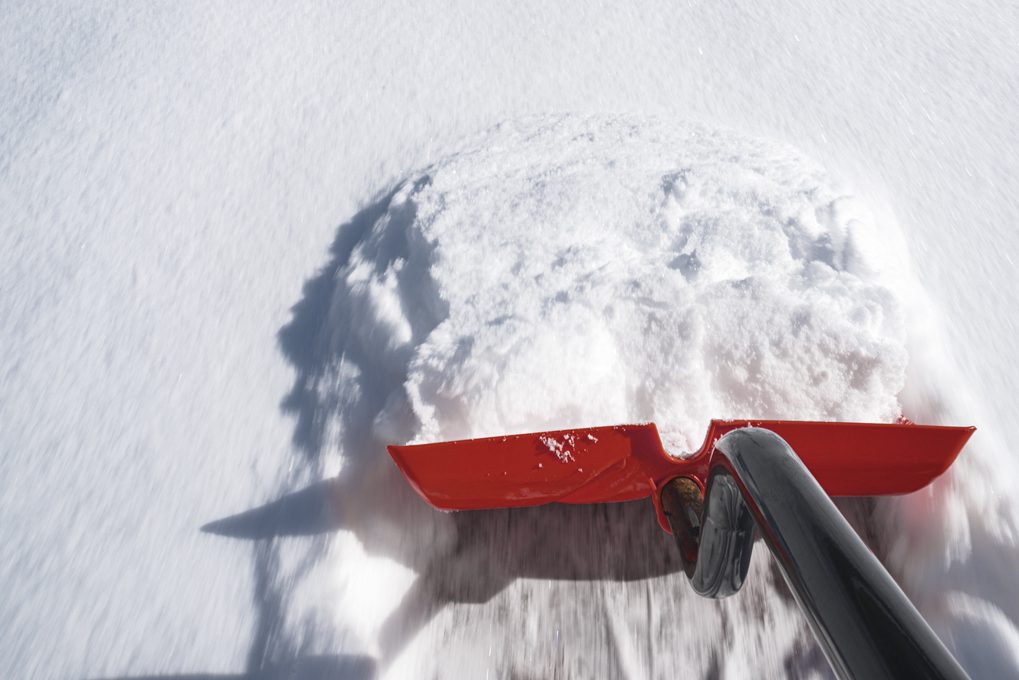 The handle of a red shovel pushing snow off of a driveway