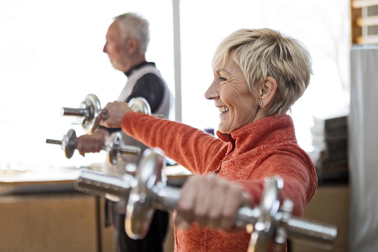 Smiling Senior couple in gym working out using dumbbell