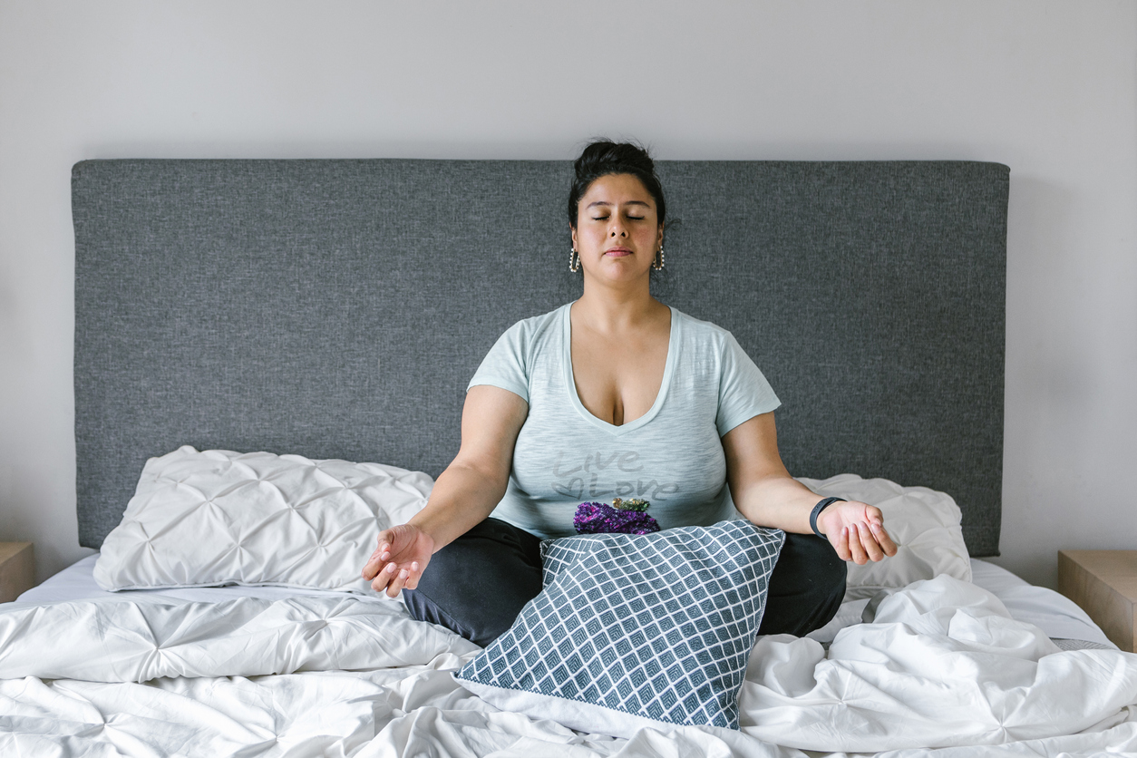 Young female meditating with closed eyes sitting on bed