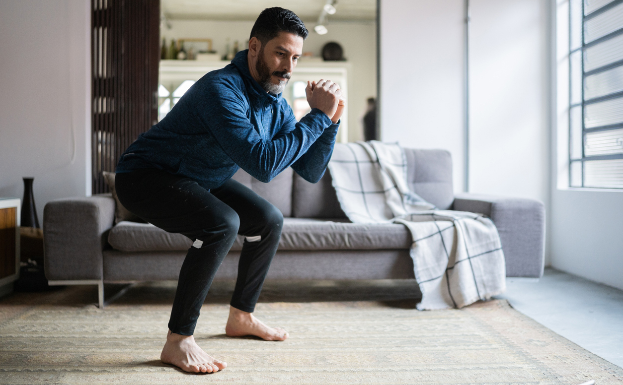Man doing squats in his living room in front of the couch