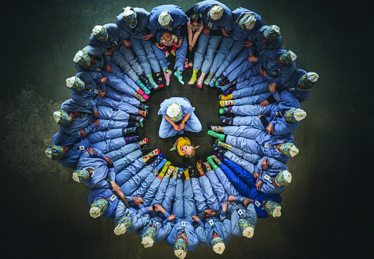 Welia Health OR team member sitting on the floor in a circle with baby Amelia in the center