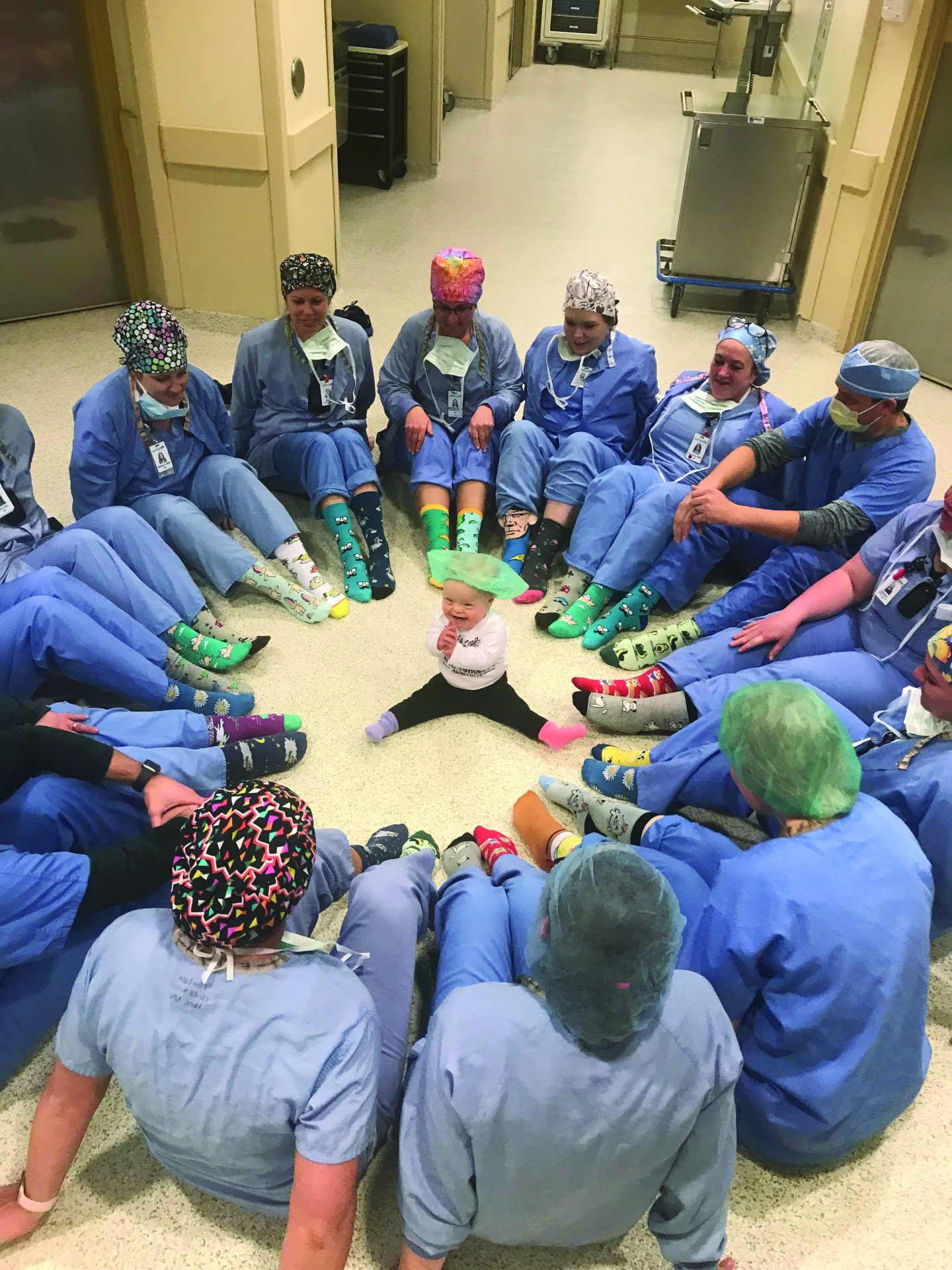 Welia Health OR team member sitting on the floor in a circle with baby Amelia in the center