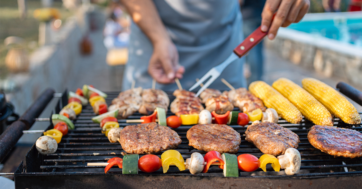 Close-up of a grill with kabobs, ears of corn and turkey burgers