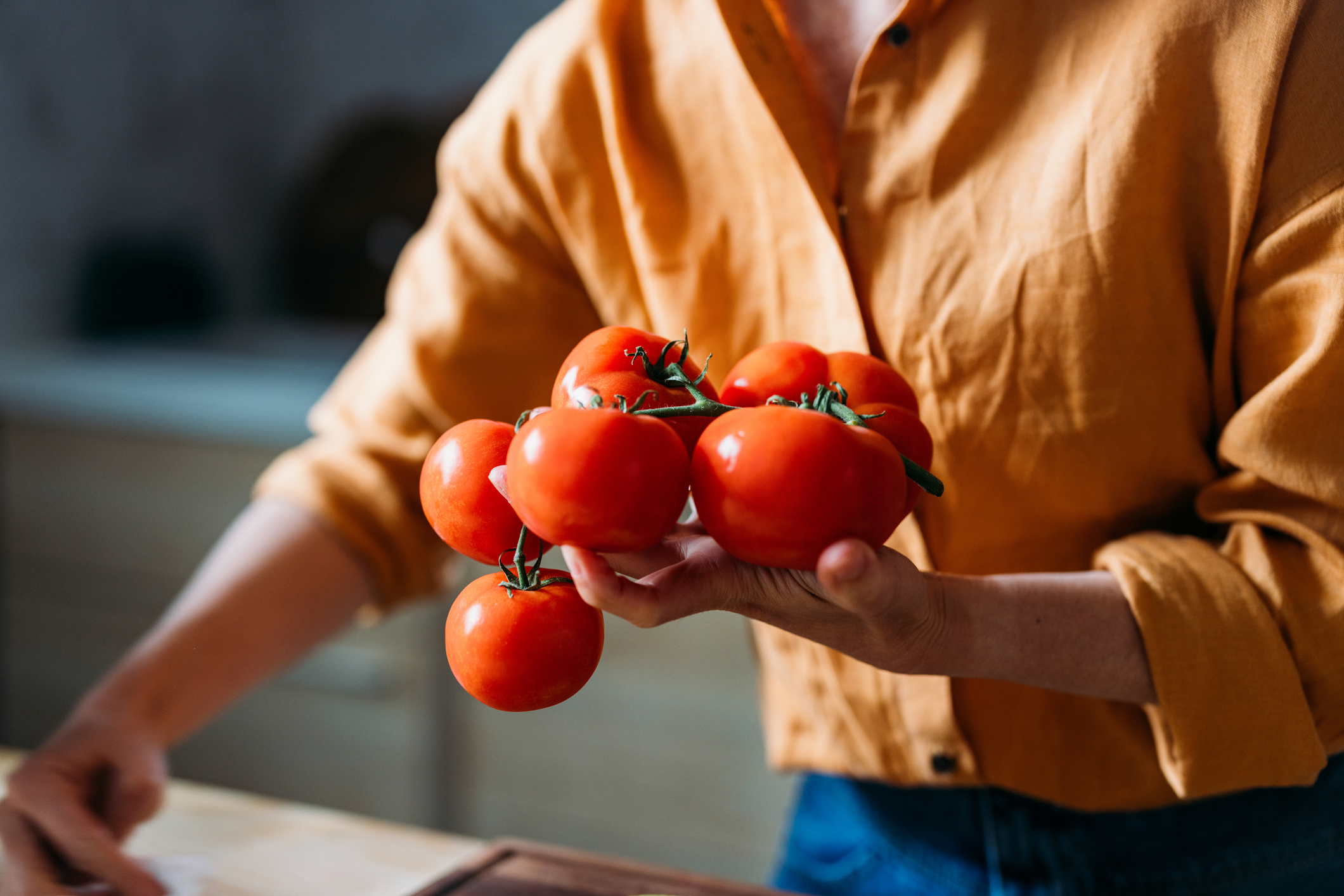 Close-up of a person holding a bunch of fresh tomatoes on the vine in a warm, cozy kitchen setting.