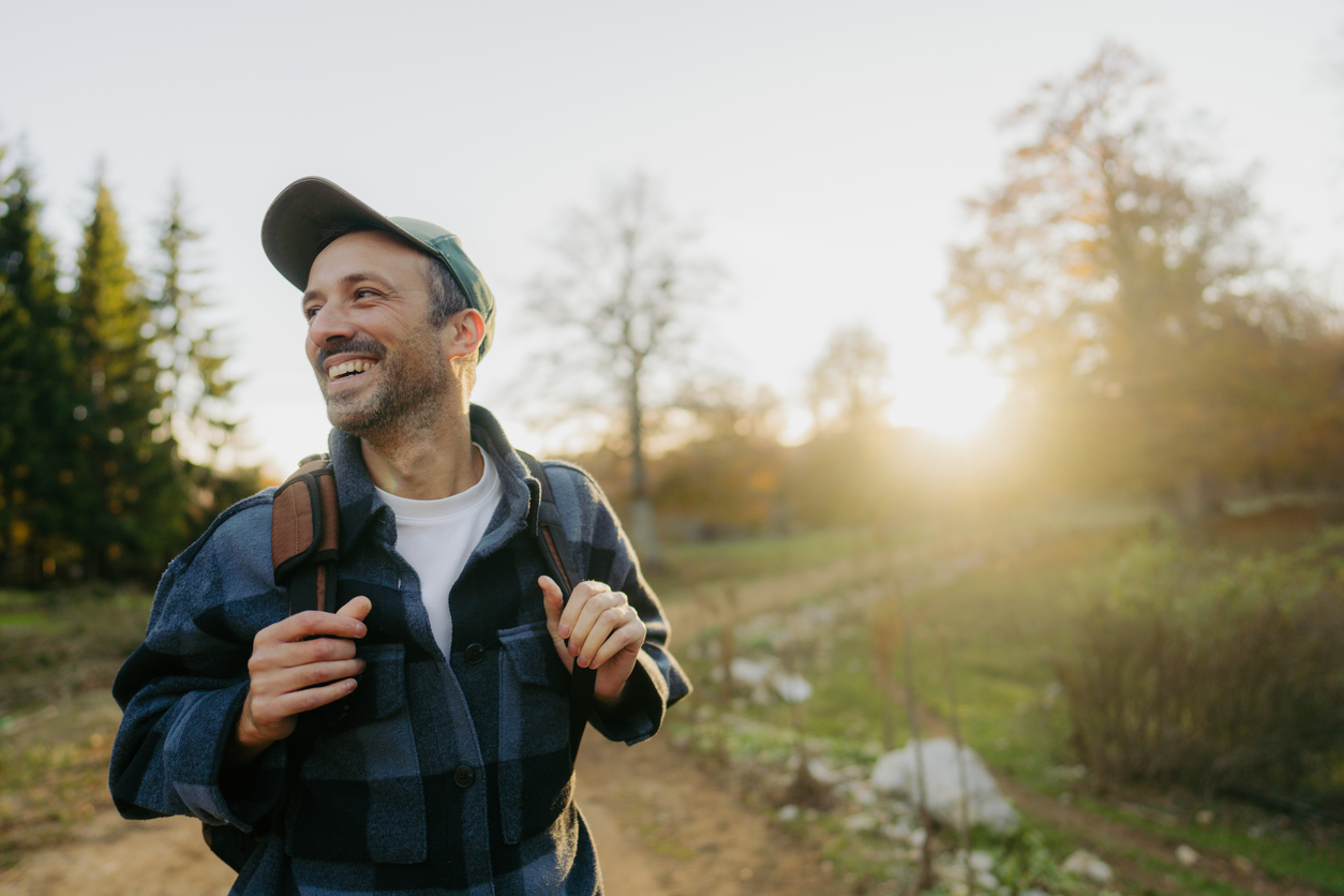 Man walking outside on a trail, carrying backpack and smiling