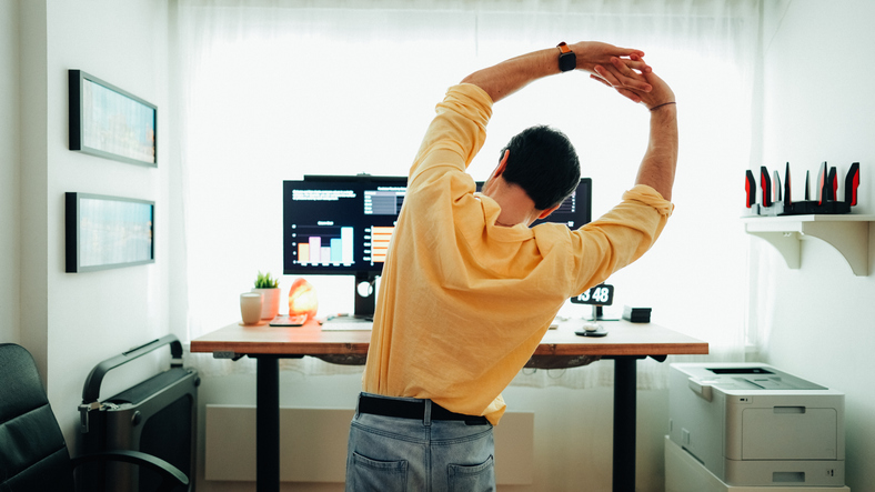 Man standing at a desk streching his arms over his head