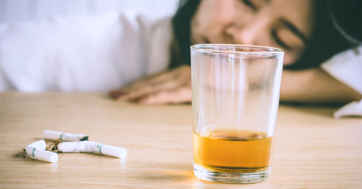 Exhausted young woman. In the foreground is a near empty glass of alcohol and several smashed cigarettes