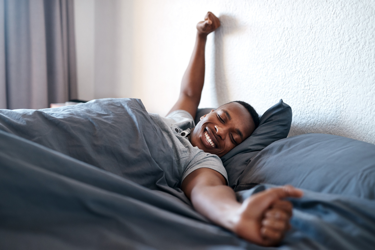 Young man waking up in bed stretching and feeling refreshed