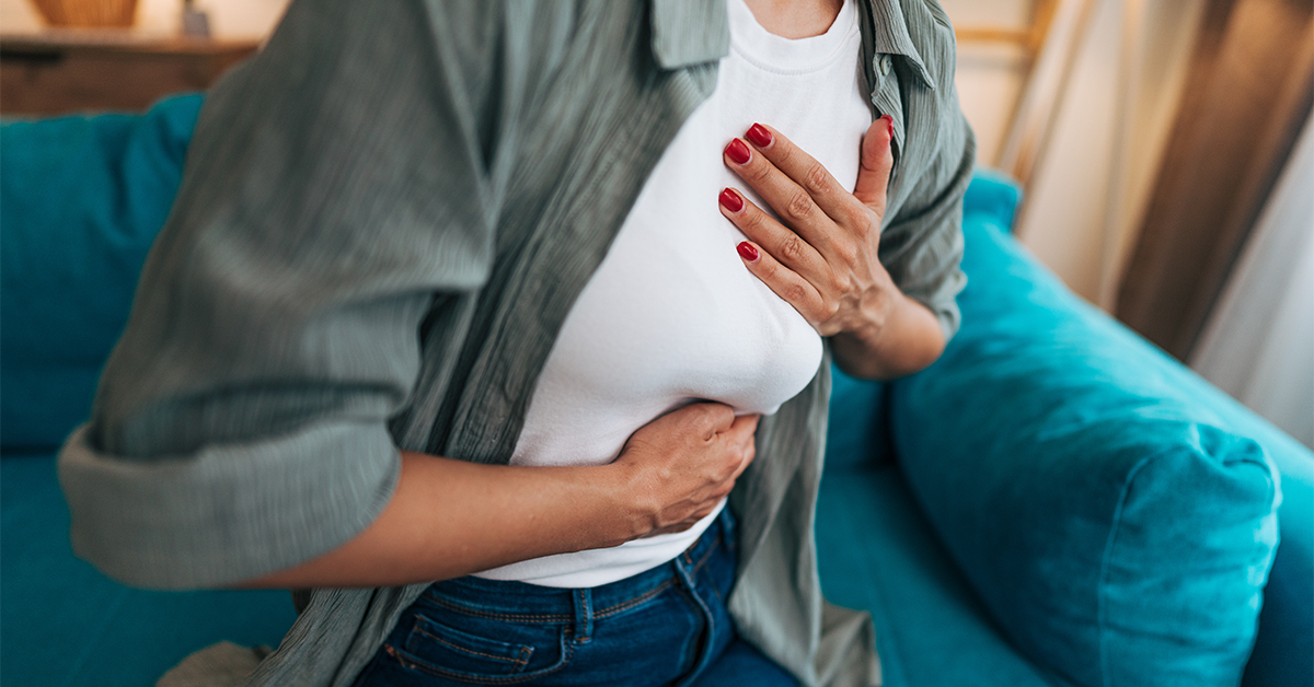 woman experiencing sudden chest pain and breathing difficulties, clutching her chest and stomach while sitting on a sofa