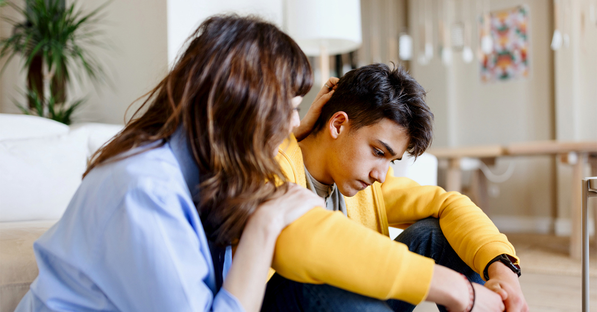 A mother sitting on the floor comforting her teenage son