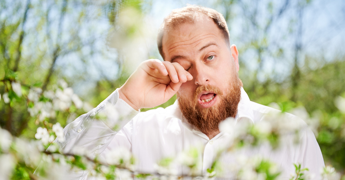 Man with itchy eyes standing among blooming trees