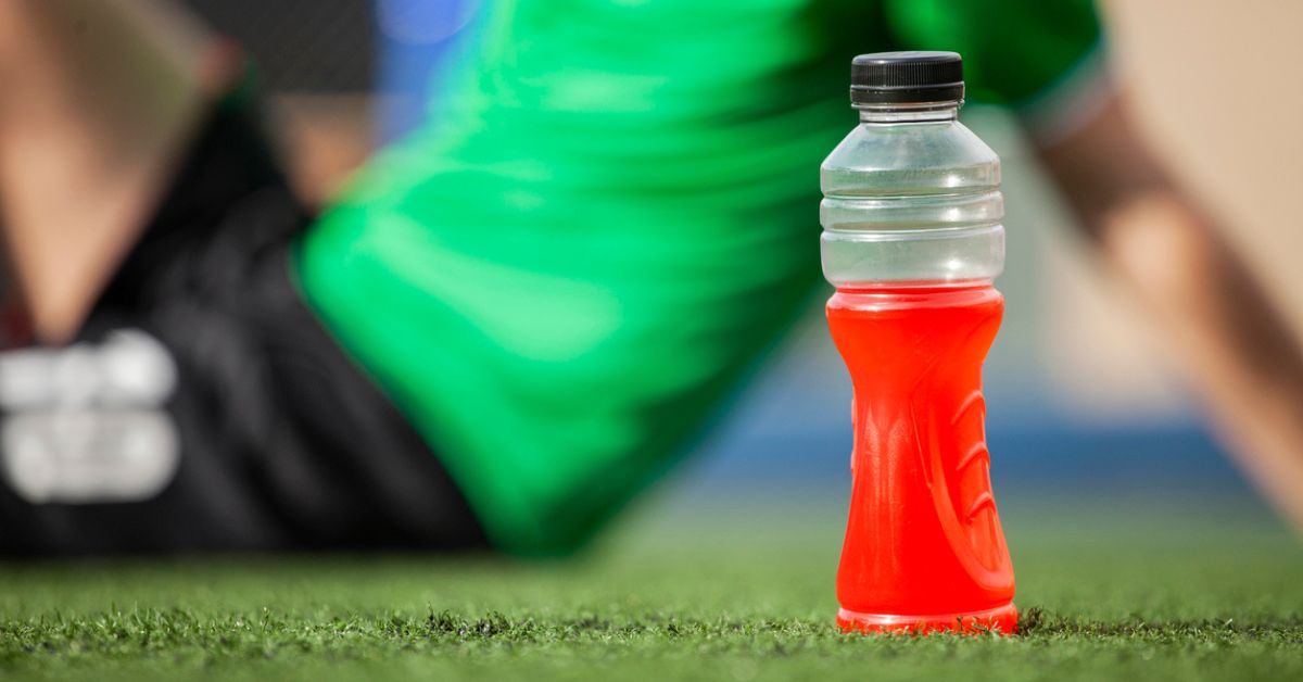 A male athlete sitting on the playing field with a sports drink in the foreground